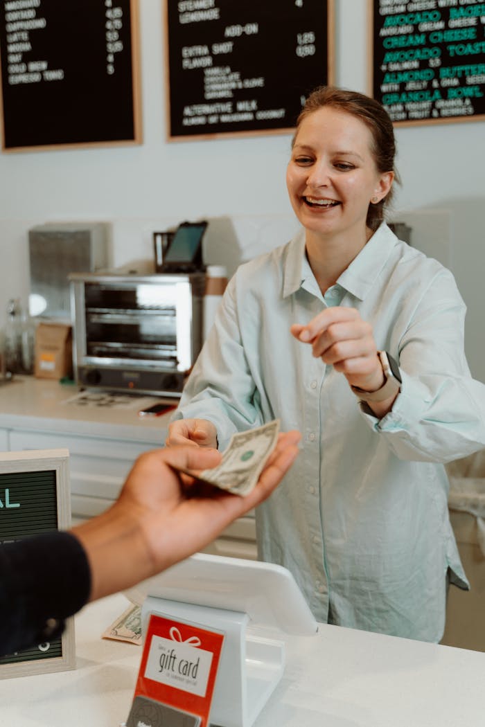 A cheerful barista receiving cash from a customer at a modern cafe counter, promoting a welcoming atmosphere.